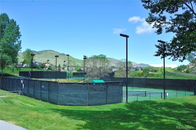 view of tennis court with a lawn and a mountain view