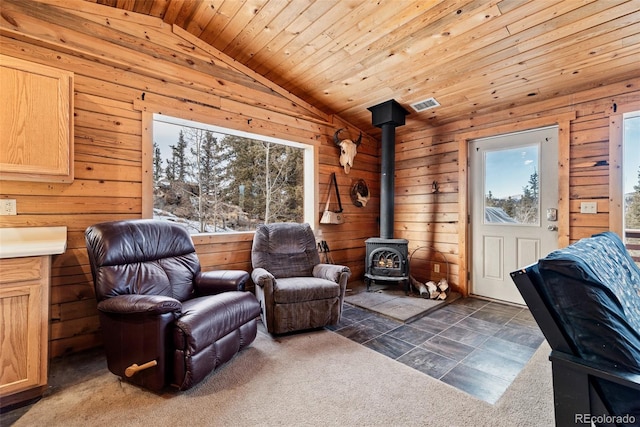 living area featuring wooden ceiling, wooden walls, visible vents, vaulted ceiling, and a wood stove