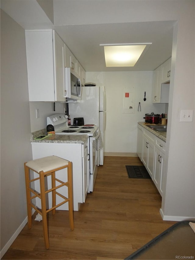 kitchen with stainless steel microwave, baseboards, wood finished floors, white cabinets, and white electric stove