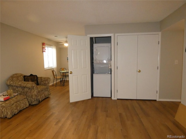 interior space featuring stacked washing maching and dryer, a ceiling fan, baseboards, and wood finished floors