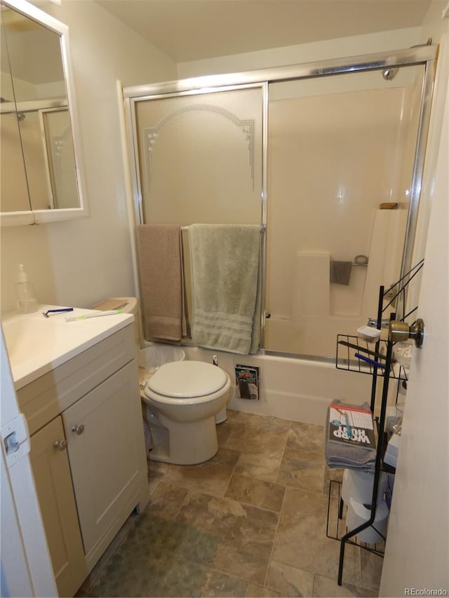 full bathroom featuring stone finish floor, toilet, vanity, and bath / shower combo with glass door