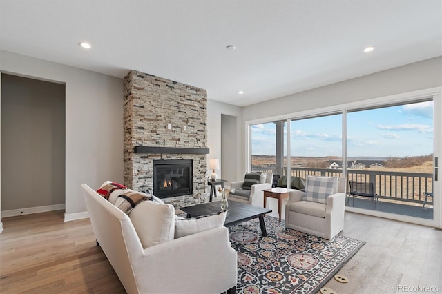 living area featuring a stone fireplace, baseboards, light wood-type flooring, and recessed lighting