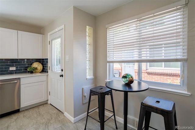 kitchen with decorative backsplash, white cabinetry, light countertops, and stainless steel dishwasher