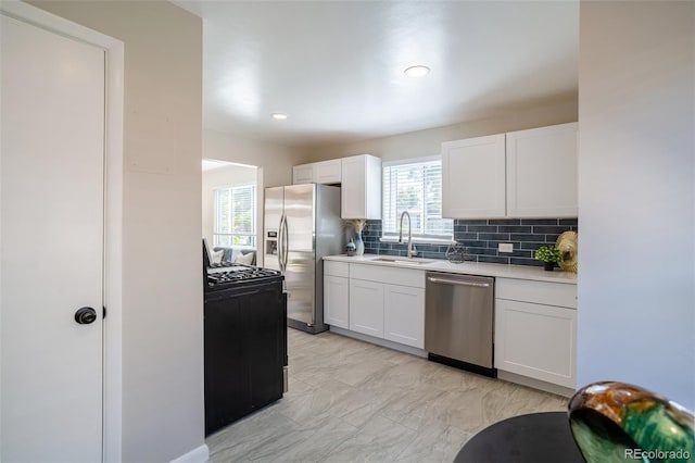 kitchen with backsplash, light countertops, appliances with stainless steel finishes, white cabinets, and a sink