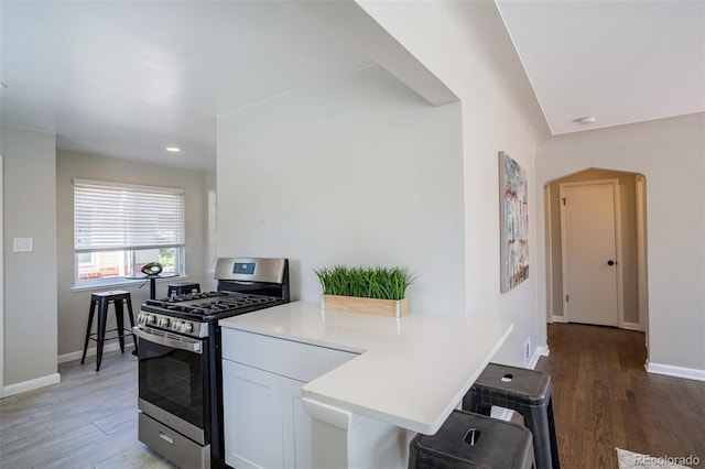 kitchen with white cabinetry, gas range, a breakfast bar area, light countertops, and baseboards