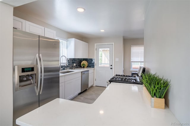 kitchen featuring backsplash, light countertops, white cabinets, stainless steel appliances, and a sink