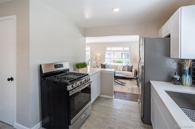 kitchen featuring stainless steel gas range oven, open floor plan, white cabinets, and light countertops