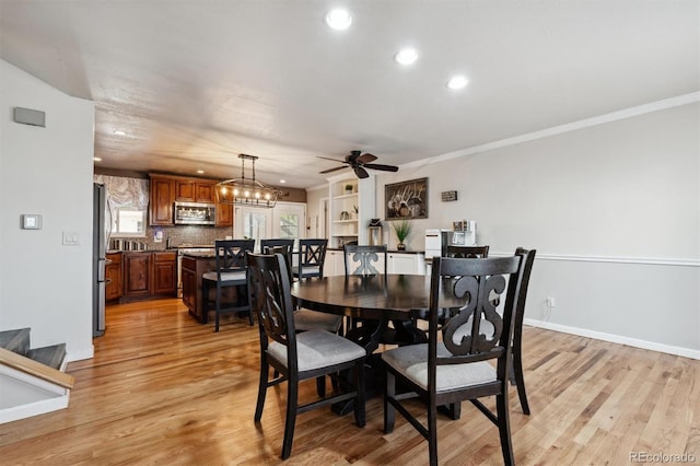 dining space with ceiling fan with notable chandelier, light wood-type flooring, and crown molding