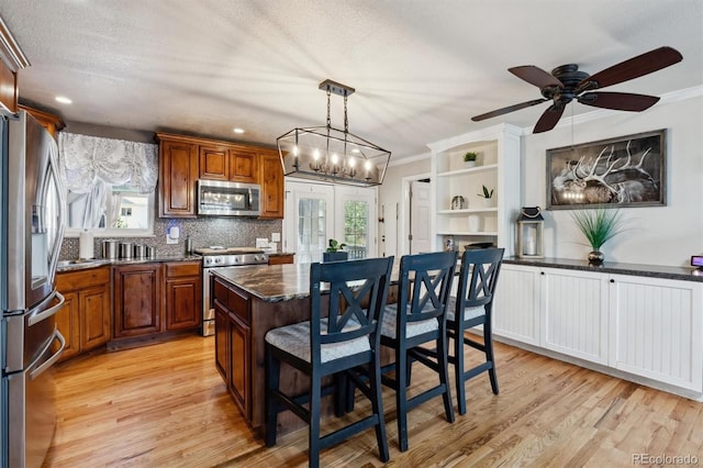 kitchen with pendant lighting, light wood-type flooring, a kitchen bar, appliances with stainless steel finishes, and ornamental molding