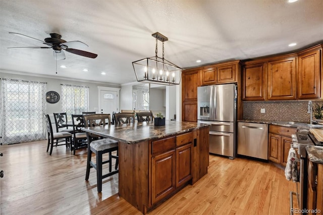 kitchen featuring appliances with stainless steel finishes, a kitchen breakfast bar, decorative light fixtures, light hardwood / wood-style floors, and a kitchen island