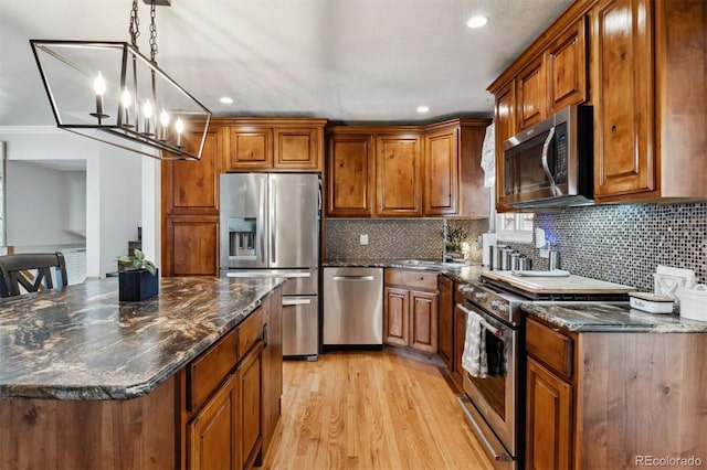 kitchen featuring appliances with stainless steel finishes, dark stone countertops, a chandelier, light hardwood / wood-style floors, and hanging light fixtures