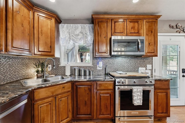 kitchen with sink, dark stone countertops, light wood-type flooring, appliances with stainless steel finishes, and tasteful backsplash