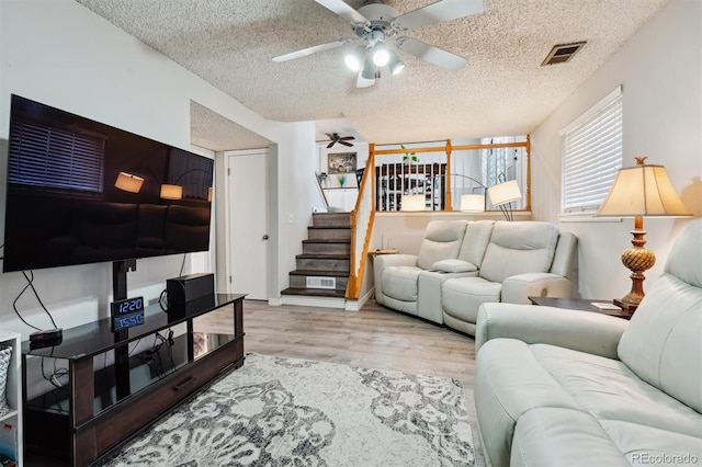 living room featuring ceiling fan, light wood-type flooring, and a textured ceiling