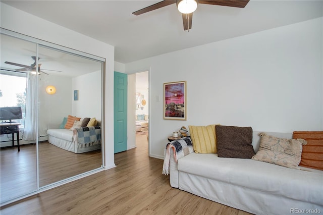 living room with a baseboard heating unit, baseboards, light wood-type flooring, and ceiling fan