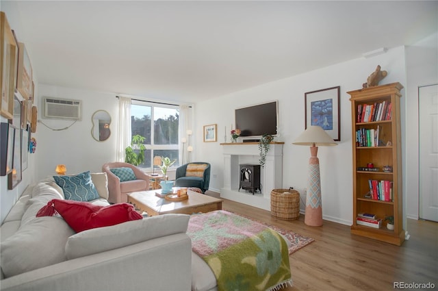 living room featuring an AC wall unit, wood finished floors, baseboards, and a fireplace with raised hearth