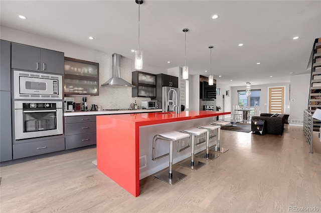 4156 Vrain St, Denver, CO 80212 - kitchen with stainless steel appliances, wall chimney exhaust hood, light wood-style flooring, a kitchen bar, and decorative light fixtures