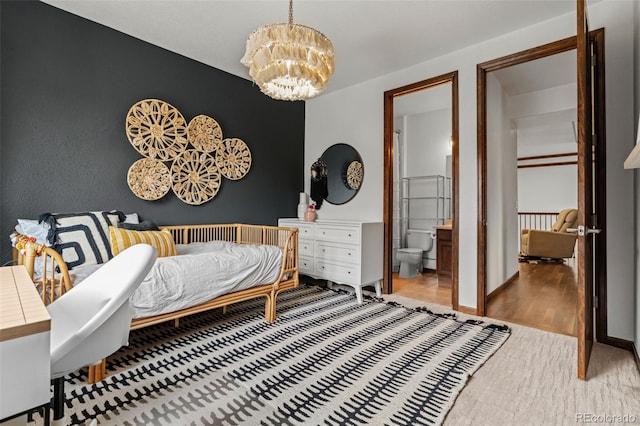 carpeted bedroom with a chandelier, ensuite bath, baseboards, and wood finished floors