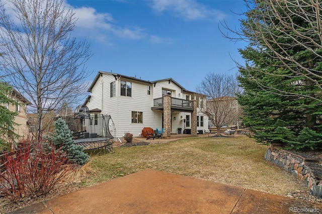 rear view of property with a trampoline, a balcony, a yard, and a patio