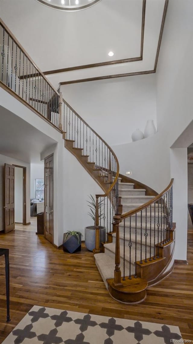 stairway with wood finished floors, a towering ceiling, baseboards, and recessed lighting
