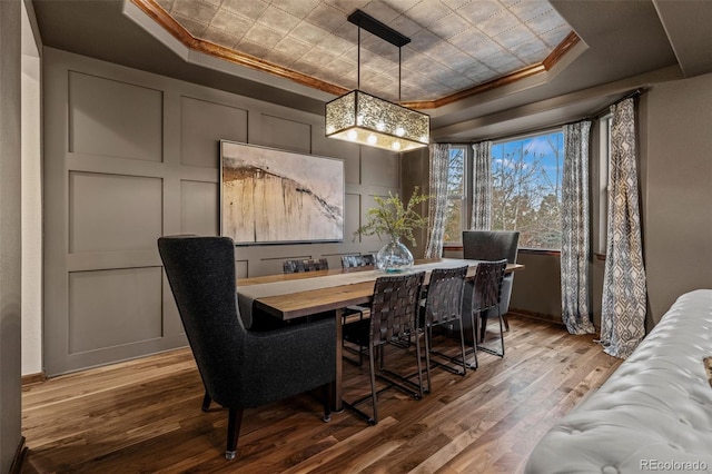 dining area with a raised ceiling, crown molding, wood finished floors, and a chandelier