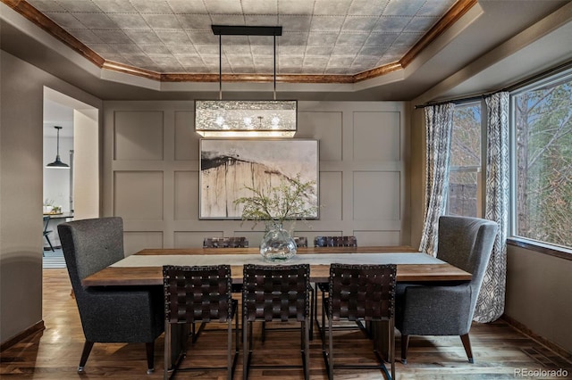 dining room with a raised ceiling, crown molding, wood finished floors, baseboards, and a decorative wall