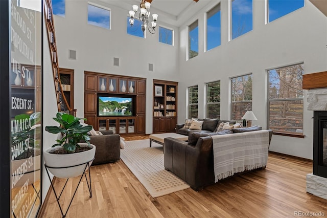 living room featuring a glass covered fireplace, light wood-style flooring, a chandelier, and a towering ceiling