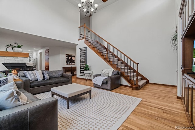 living area with stairway, light wood-type flooring, a fireplace, a towering ceiling, and a chandelier