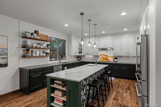 kitchen with open shelves, appliances with stainless steel finishes, a sink, a center island with sink, and white cabinets