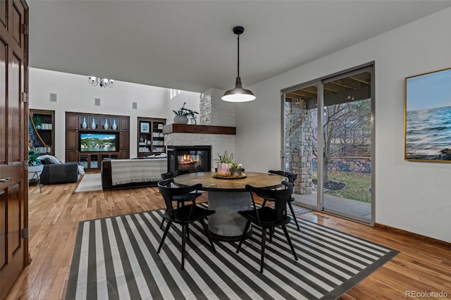 dining area with light wood-style flooring, a stone fireplace, and a chandelier