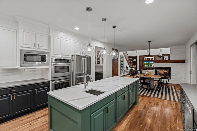 kitchen featuring green cabinetry, stainless steel appliances, a sink, white cabinetry, and a center island with sink