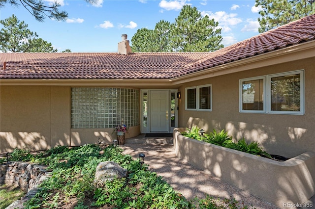 property entrance with a tile roof, stucco siding, and a chimney