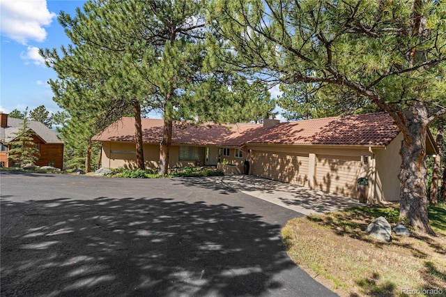 single story home with asphalt driveway, a tile roof, stucco siding, a garage, and a chimney
