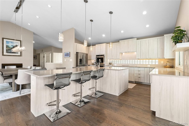 kitchen with appliances with stainless steel finishes, vaulted ceiling, modern cabinets, a large island with sink, and tasteful backsplash