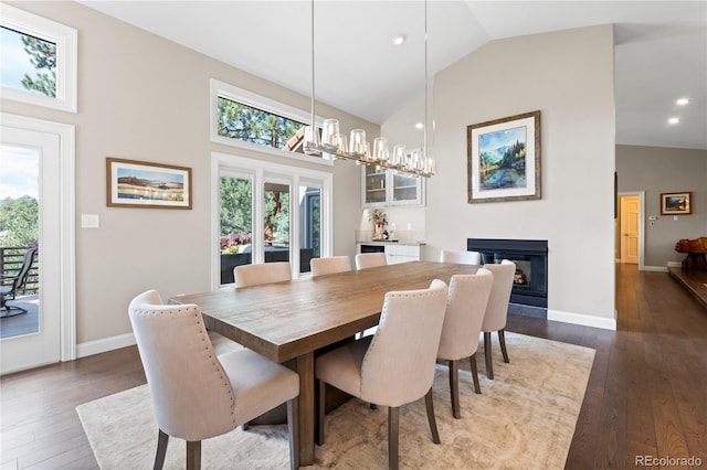 dining room featuring dark wood finished floors, a glass covered fireplace, high vaulted ceiling, and plenty of natural light