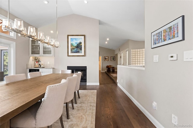 dining room featuring lofted ceiling, dark wood-style floors, a glass covered fireplace, baseboards, and recessed lighting