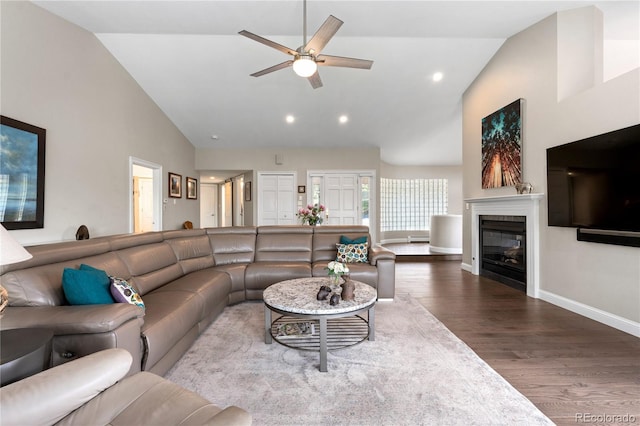 living room with wood finished floors, a ceiling fan, a glass covered fireplace, baseboards, and high vaulted ceiling