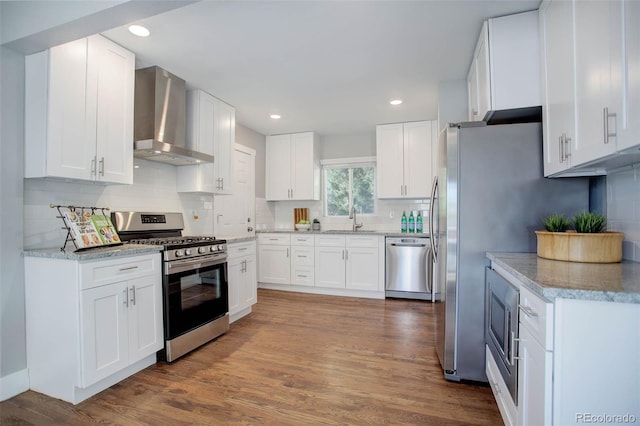 kitchen featuring white cabinetry, sink, stainless steel appliances, wall chimney range hood, and hardwood / wood-style floors