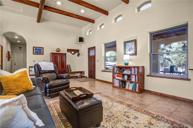 tiled living area featuring arched walkways, beam ceiling, and baseboards