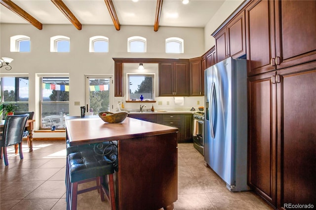 kitchen with light tile patterned floors, a breakfast bar area, a high ceiling, a sink, and appliances with stainless steel finishes