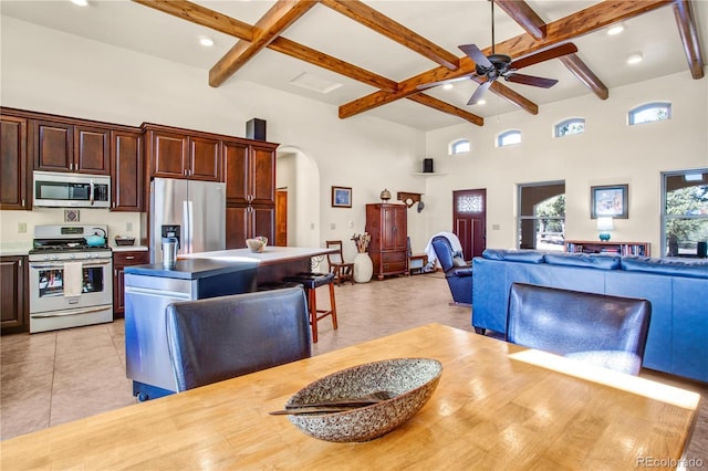 kitchen with arched walkways, a center island, stainless steel appliances, a towering ceiling, and open floor plan