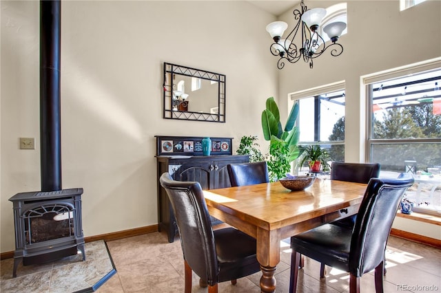 dining room featuring a notable chandelier, light tile patterned floors, a wood stove, and baseboards