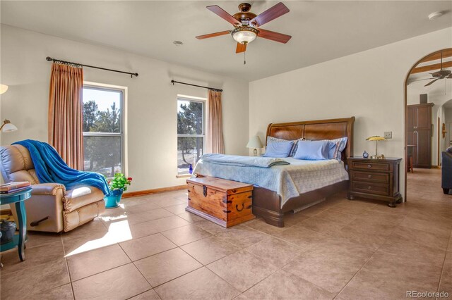 bedroom with light tile patterned floors, ceiling fan, arched walkways, and baseboards