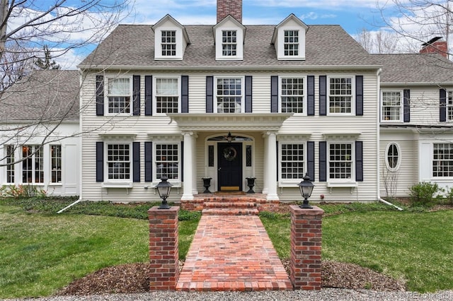 colonial inspired home featuring a chimney, a front lawn, and a shingled roof