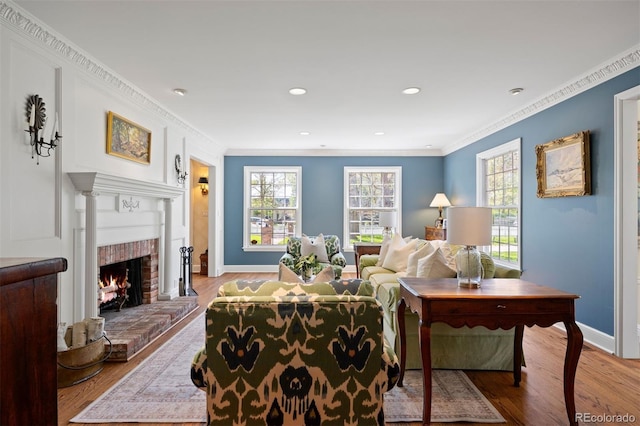 living room featuring light wood-style flooring, baseboards, a fireplace, crown molding, and recessed lighting