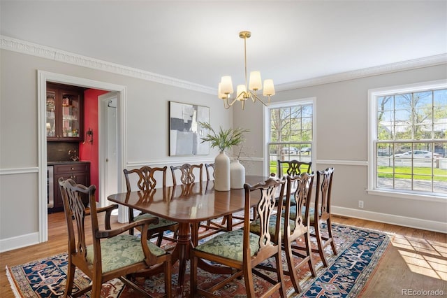 dining space with a chandelier, ornamental molding, light wood-style flooring, and baseboards