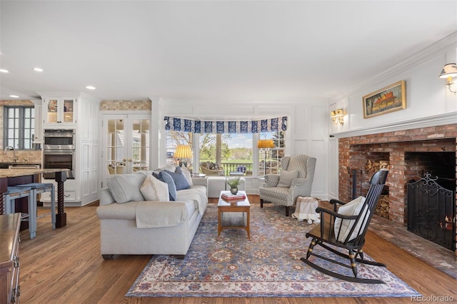 living room with a brick fireplace, ornamental molding, dark wood finished floors, french doors, and recessed lighting