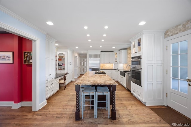 kitchen with stainless steel appliances, white cabinets, recessed lighting, wood finished floors, and glass insert cabinets