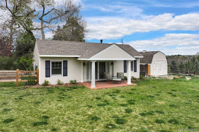 rear view of house featuring a storage shed, a patio, a shingled roof, and an outdoor structure