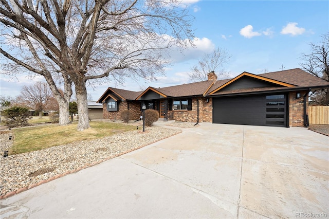 view of front facade with driveway, brick siding, an attached garage, and a chimney