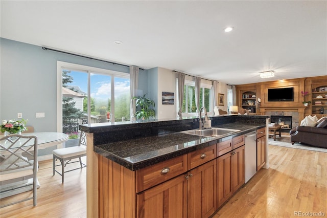 kitchen featuring a sink, dishwasher, light wood-style floors, a glass covered fireplace, and open floor plan